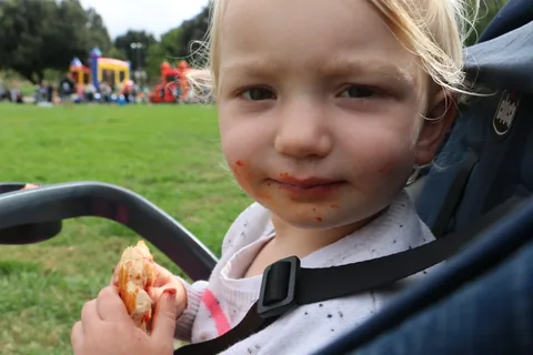 A toddler eating a snack looks up with a slightly messy face.