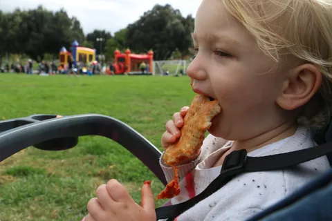 A young child happily eats a treat at the outdoor event