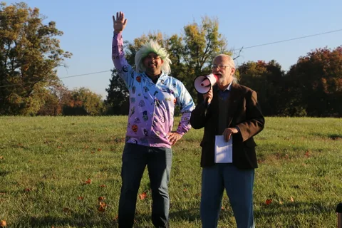 A woman in a tie-dye jacket waves next to a man holding a megaphone under the balloon.