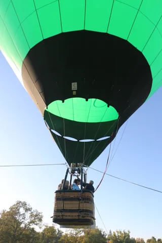 The balloon basket rises against a clear blue sky with two riders aboard.