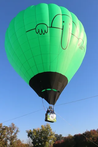 A green hot air balloon rises against a clear blue sky