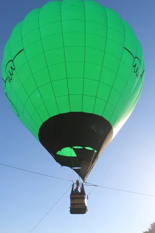 A green hot air balloon envelope fills the frame against the sky.