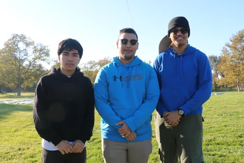 Three young men in hoodies pose together on the grass after their balloon ride.