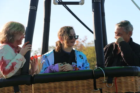Guests in zombie makeup ride the tethered hot air balloon basket, laughing together in golden light.