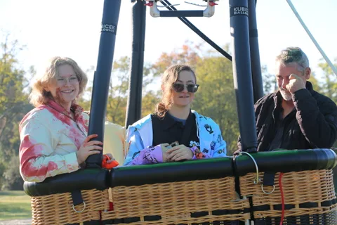 Riders chat in the hot air balloon basket in warm morning light.