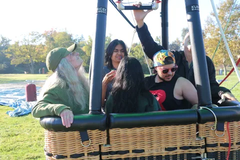 An older woman laughs skyward while riders gather in the balloon basket.