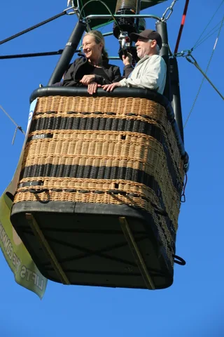 Riders look down from the balloon basket against the sky.