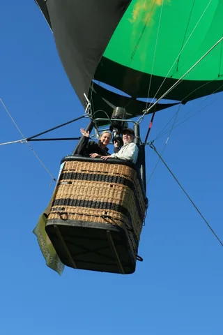 Riders in the balloon basket seen from below against the sky.