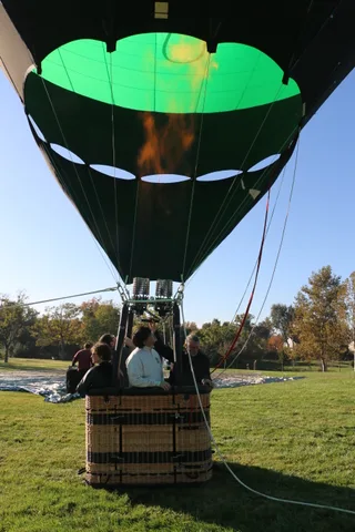 Riders lean over the balloon basket edge, smiling down at the ground crew.