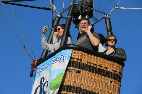 Riders wave from the balloon basket beside the Davis Food Co-op banner.