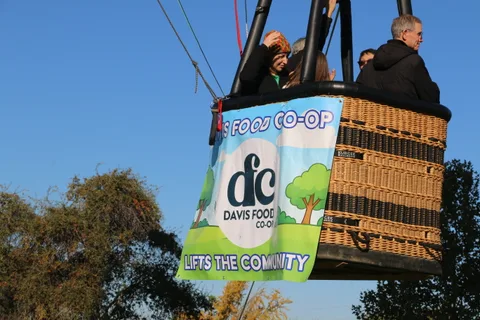 The balloon rises against the sky, its Davis Food Co-op banner reading Lifts the Community.