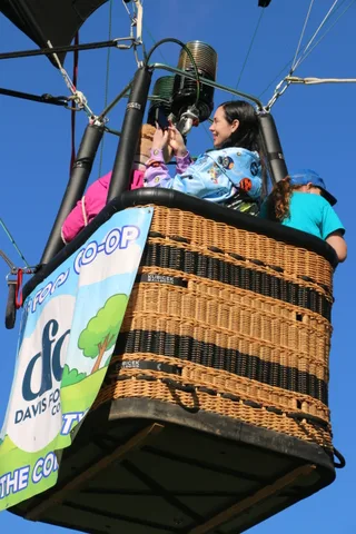 A rider photographs the view from the balloon basket beside the Davis Food Co-op banner.