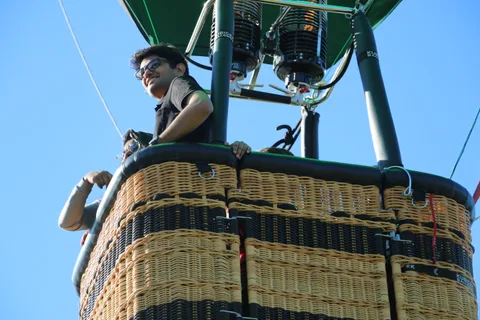 A rider works near the balloon burner controls against the sky.