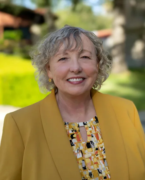 Yolo County Supervisor Sheila Allen, smiling in a yellow jacket outside a county building.