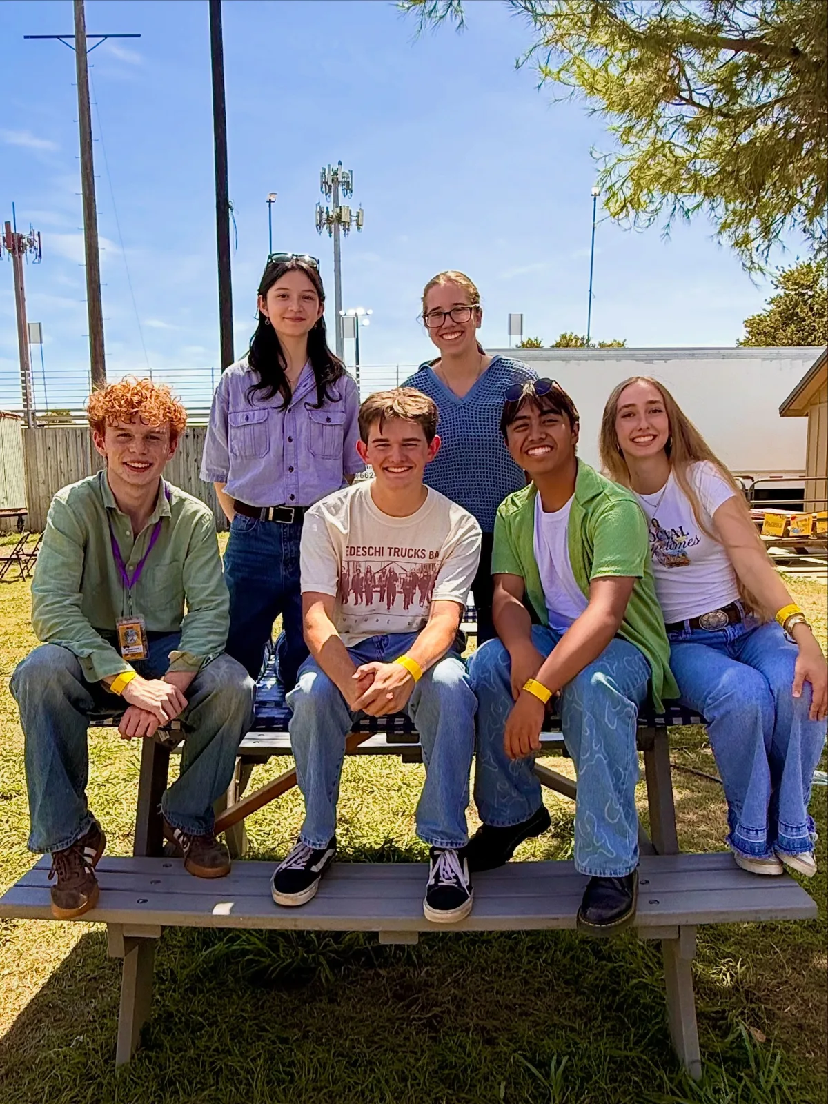 Betrayal: six of the band sitting on and around a wooden picnic table outdoors on a sunny day, smiling at the camera.