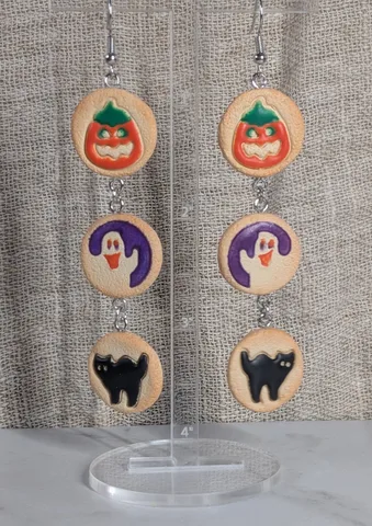 Earrings made from three stacked clay cookies each, iced with a jack o lantern, a ghost and a black cat.