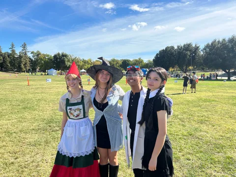 The four singers pose together in Halloween costumes on the festival field: a garden gnome, a witch, a mad scientist and Wednesday Addams.