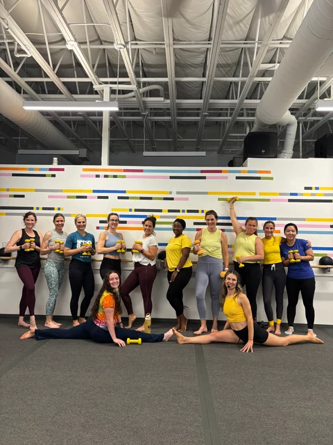 A Yolo Barre class holding light dumbbells at the barre, two members doing the splits in front