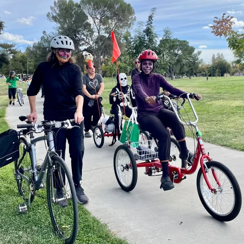 Costumed riders on the parade route, one of them on a red adaptive trike with a safety flag.