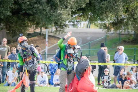 A skydiver bundles a canopy beside the taped crowd line.
