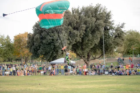 A skydiver touches down on the grass beside the crowd line.