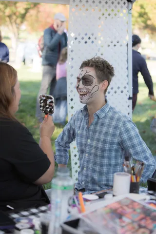A guest with face paint smiles into a hand mirror at the booth