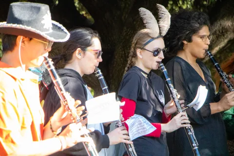 Four clarinet players in costume perform side by side under the trees.