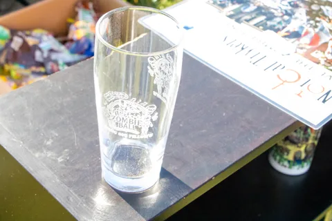 An etched commemorative pint glass on a table beside a printed card