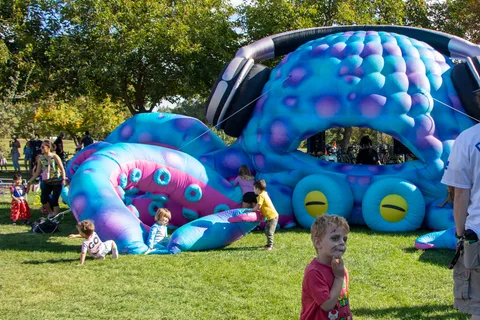 Kids playing on a giant inflatable monster bounce house at the Zombie Bike Parade festival, with a zombie-face-painted boy in the foreground