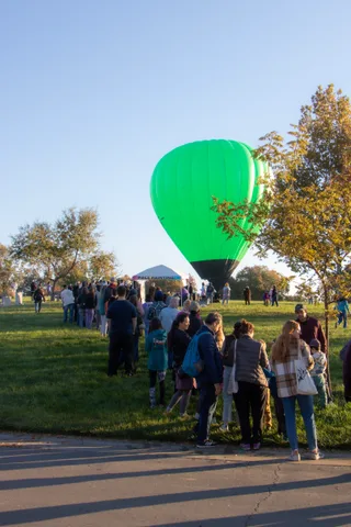A crowd on the path watches a green balloon on the field