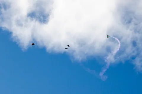 Two skydivers trail smoke as they drop past a bank of cloud.