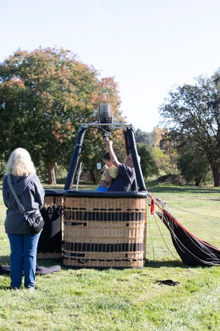 A balloon basket sits on the grass as the burner is checked