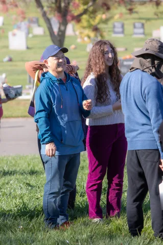 Three people stand together on the lawn with headstones behind them