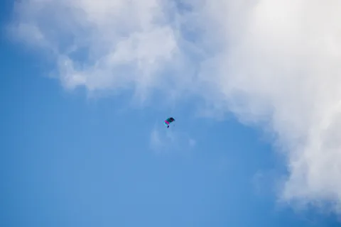 A parachute opens as a tiny figure drops out of a bank of cloud.