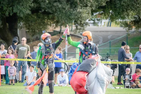 Two skydivers raise a hand to the crowd after landing.