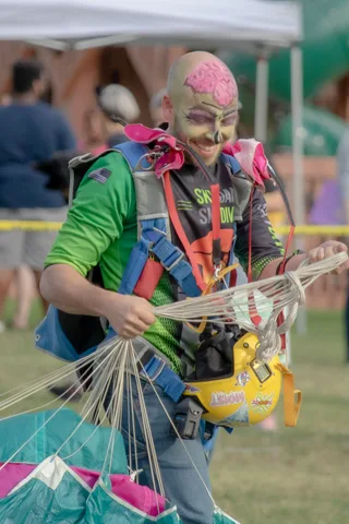 A skydiver in face paint gathers the lines of a packed canopy.