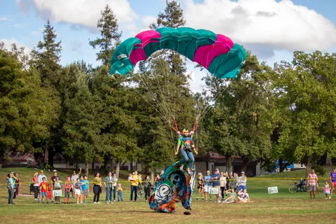 A skydiver touches down and the flag settles on the grass.