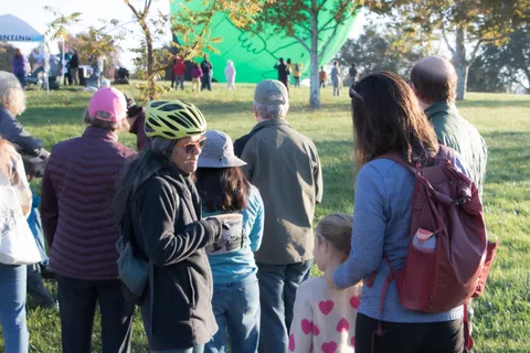 A crowd stands watching with a green balloon behind