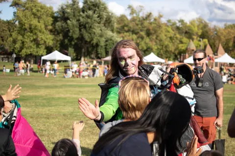 A child reaches up to high five a skydiver walking past.
