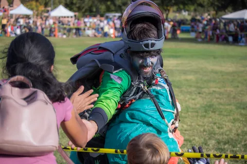 A skydiver in face paint high fives a child over the tape.