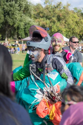 A skydiver in face paint carries a canopy through the crowd.