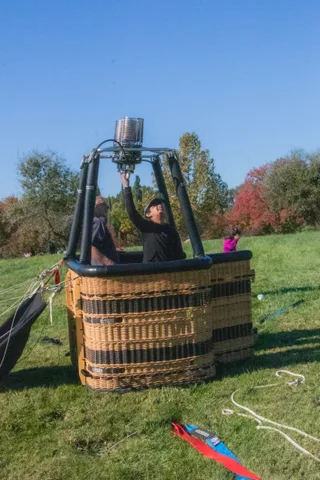 A balloon basket and burners set up on the grass before inflation