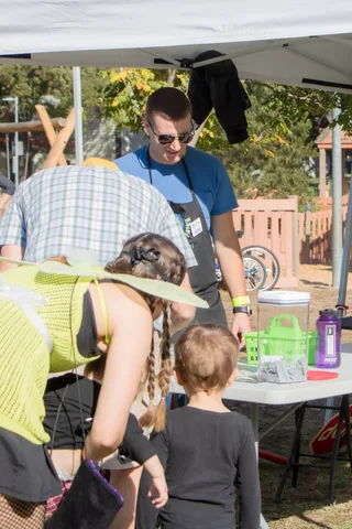Families gather around a craft table under a white canopy.