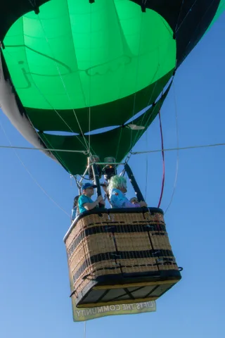 A green balloon carries its basket overhead