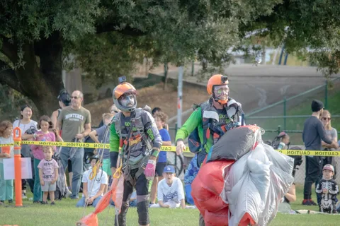 Two skydivers stand together bundling up their canopies.