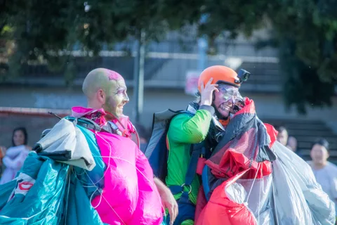 Two skydivers in face paint carry their bundled canopies.