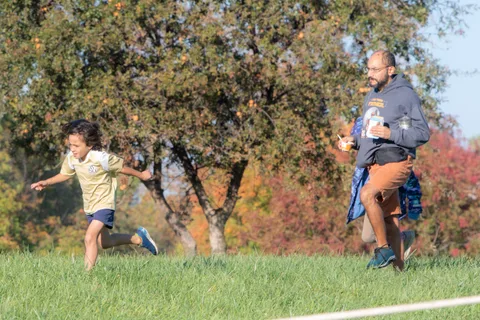 A child runs on the lawn as a person walks past under fall trees