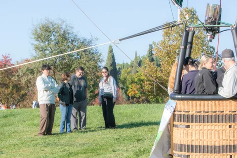 People stand around a balloon basket tethered on the grass