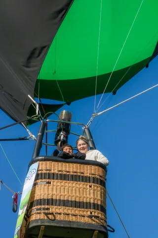 Passengers look down from a balloon basket overhead