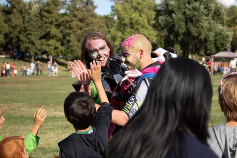Children high five two skydivers in face paint after landing.